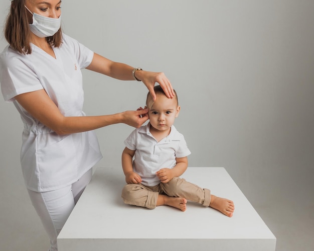Женщина-врач накладывает пластырь на лоб мальчика в помещении. студийное фото. концепция здоровья