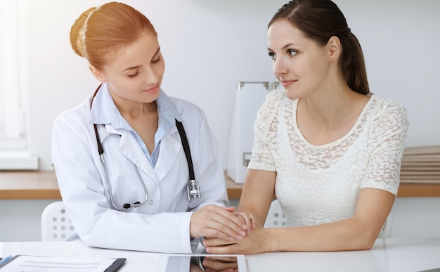 Woman-doctor reassuring her female patient while sitting at the desk. Medicine concept.