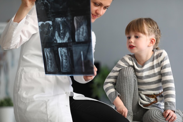 여자 의사는 어린 소녀에게 척추의 엑스레이를 보여줍니다