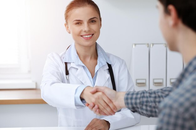 Woman-doctor smiling while shaking hands with her male patient. Medicine concept.