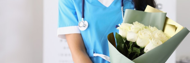 女性医師がクリニックに立ち、白いバラの花束を持っています。