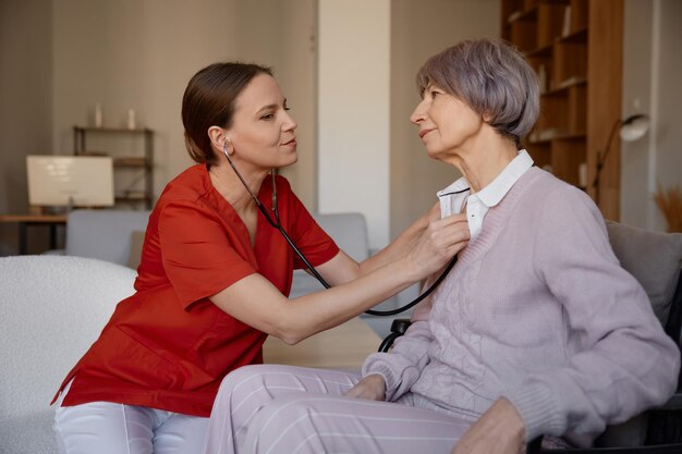 Photo woman doctor using stethoscope while examining senior woman at nursing home