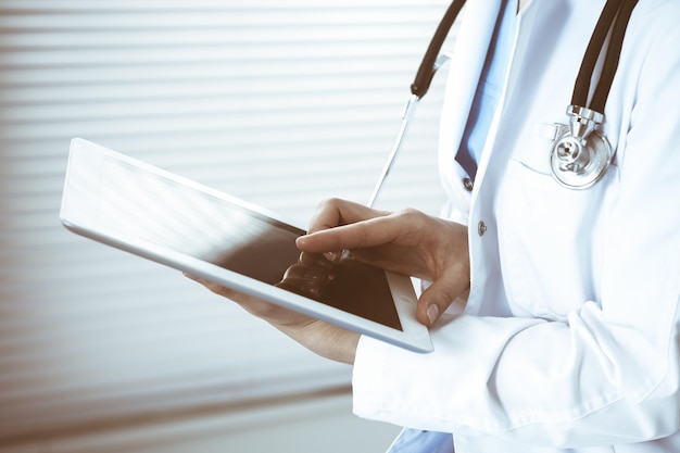 병원의 자에 앉아 있는 동안 흰색 태블릿 컴퓨터를 사용하는 여성 의사 클로즈업.