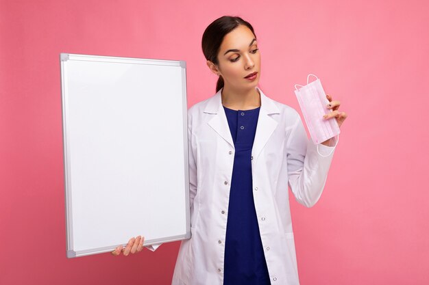 Woman doctor in a white medical coat holding blank board with copy space for text and protective