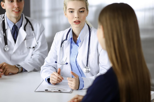 Woman-doctor with male colleague are consulting patient woman while sitting at the desk in modern clinic. Perfect medical service, medicine concept.