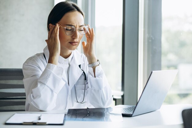 Woman doctor working on laptop and having head ache