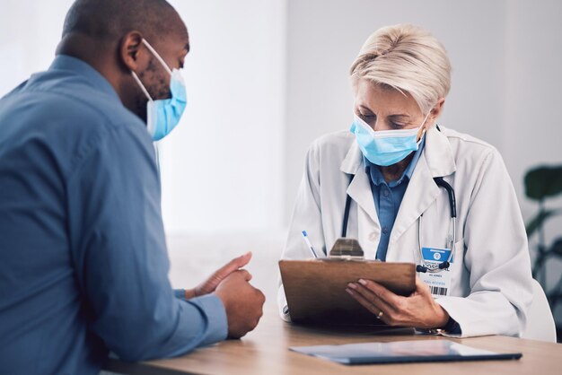 Woman doctor and writing on clipboard with patient in consultation checkup or life insurance at hospital Female person medical or healthcare expert with face mask consulting customer at clinic