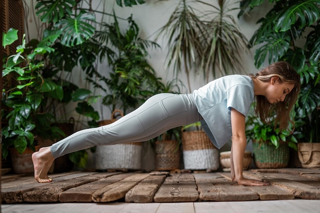 A woman does sports The trainer does yoga asana exercises Fitness at home with plants