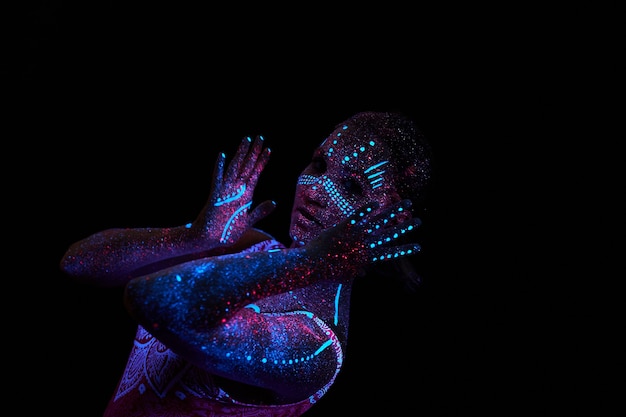 Woman does yoga, hand movement, body warm-up. Art girl cosmos in ultraviolet light. Entire body is covered with colored droplets. Astral yoga. Noise, out of focus