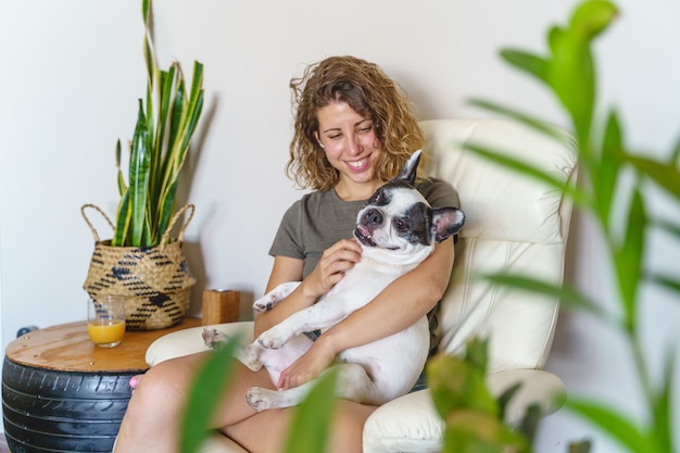 家でブルドッグと女犬愛好家。植物で隔離の犬をくすぐる女性の水平方向のビュー。