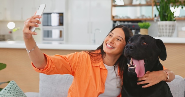 自宅のリビングルームのソファで女性の犬と自撮り写真をケアし、幸せな友達を抱擁し、抱擁します。犬のお母さんのソファとペット動物のラウンジ、または笑顔でリラックスして写真撮影できるソーシャルメディアアプリ