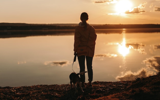 Женщина и собака смотрят закат на берегу моря