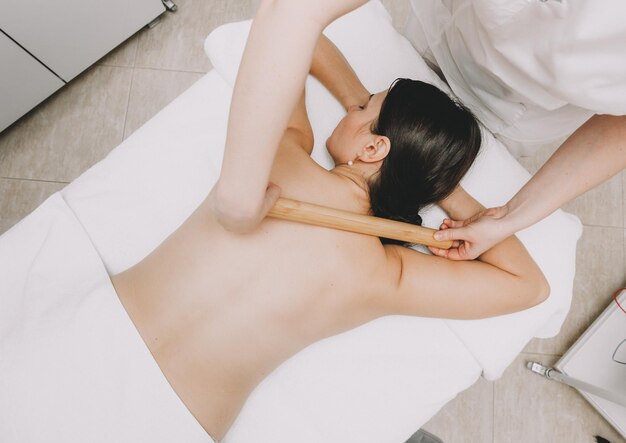 Woman doing back massage with bamboo stick in wellness spa center