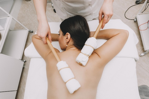 Woman doing back massage with bamboo stick in wellness spa center