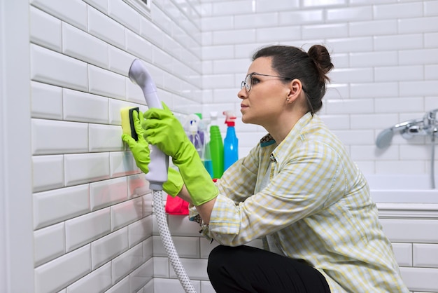 Женщина делает уборку ванной дома, женская стиральная плитка на стене с паром. Использование пароочистителя для быстрой очистки