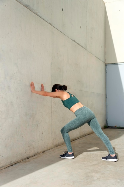 Woman doing a calf or leg stretch against a concrete wall outside warm up exercises