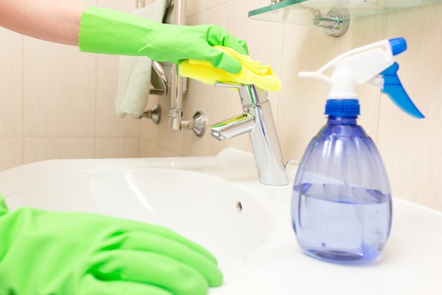 Woman doing chores in bathroom, cleaning sink and faucet with spray.