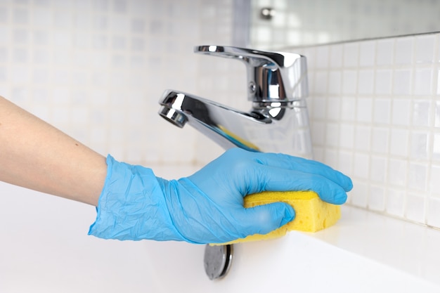 Woman doing chores in bathroom cleaning of water tap with sponge