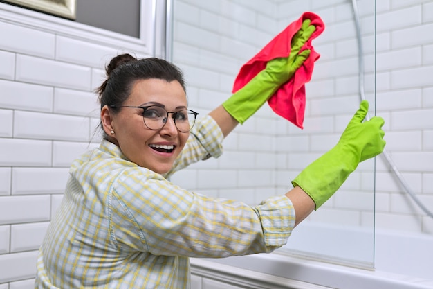 Woman doing cleaning in the bathroom, at home. Female cleaning polishing shower glass with a washcloth with microfiber.