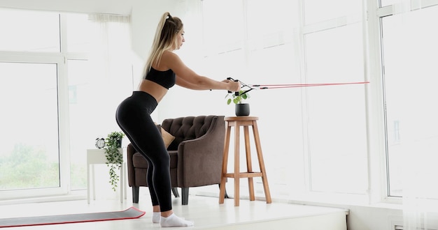 A woman doing exercises in a room with a chair and a window