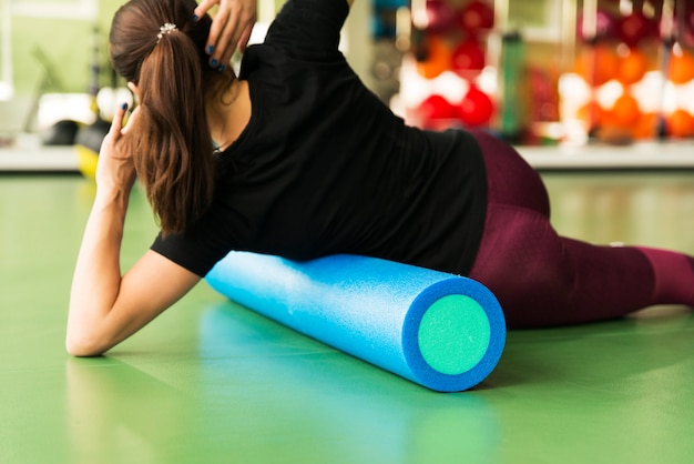 Woman doing foam roller exercise on a floor in gym