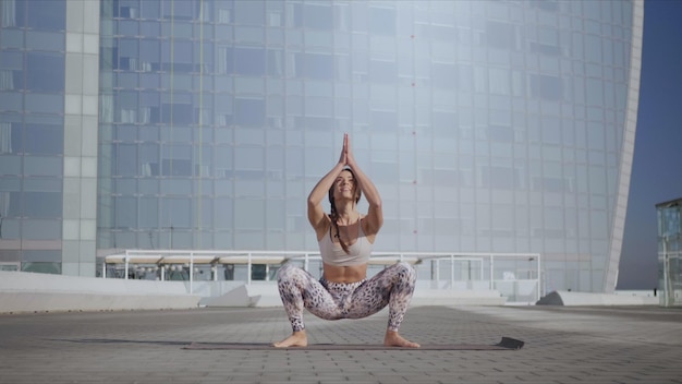 Woman doing garland pose on yoga mat at street Yoga trainer exercising outside