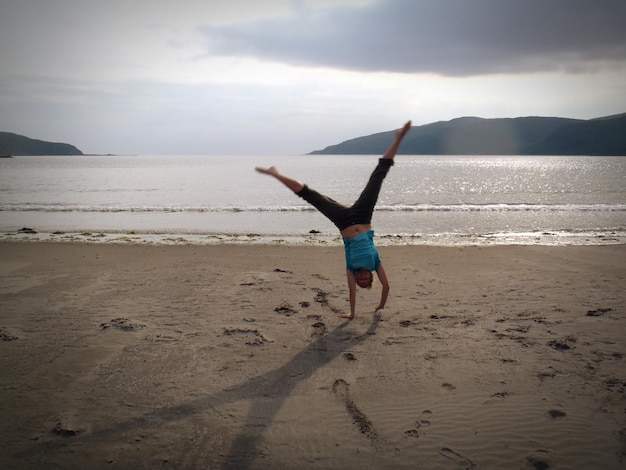 woman doing handstand at beach against sky