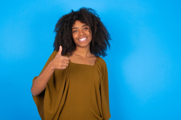 Woman doing happy thumbs up gesture with hand approving expression looking at the camera showing