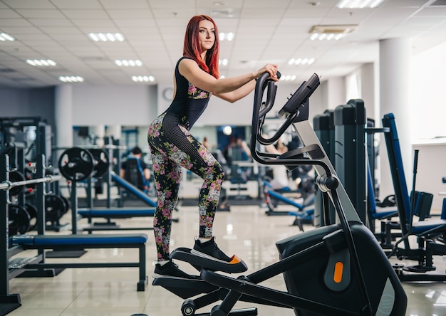 Woman doing legs exercise on stair steppers machine, in gym