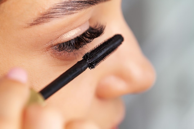 Woman doing morning makeup routine putting mascara in bathroom mirror at home