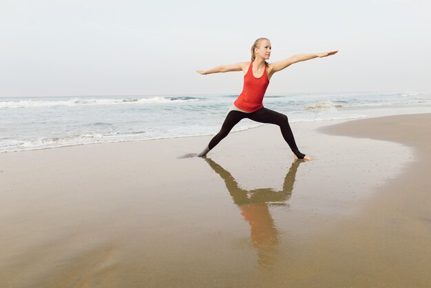 Woman doing morning yoga on the beach near the sea with reflection in the water