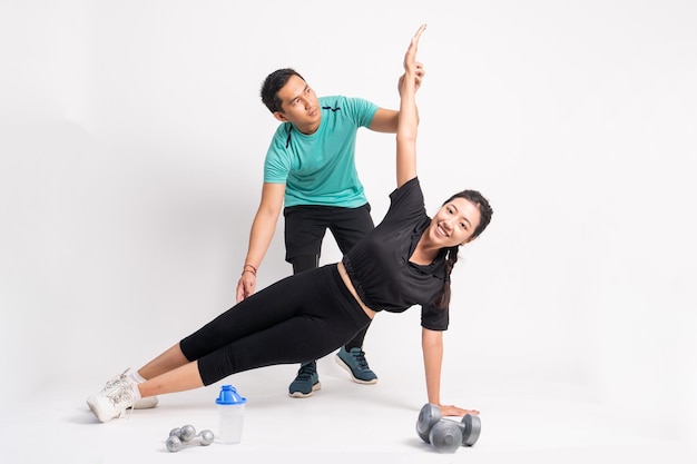 Woman doing side plank with trainer holding legs and arms