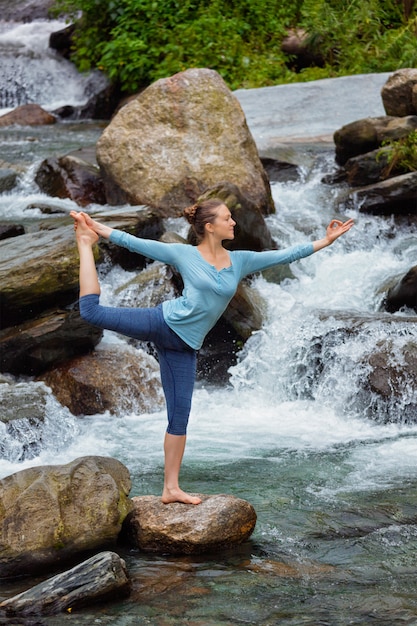 Woman doing yoga asana Natarajasana outdoors at waterfall