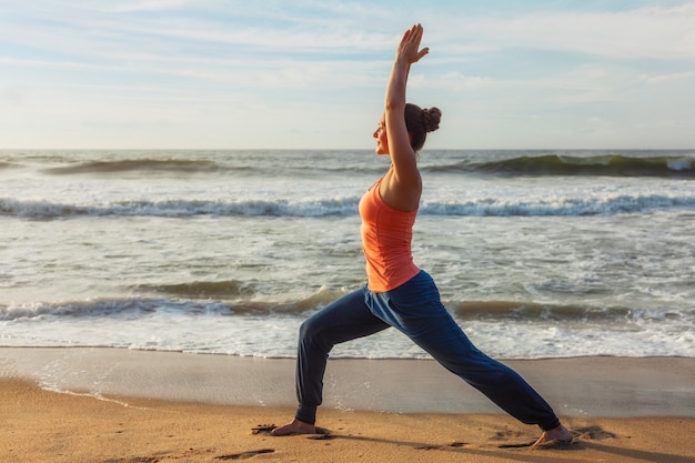 요가 아사 나 Virabhadrasana 1 전사 포즈를 하 고 해변에 여자