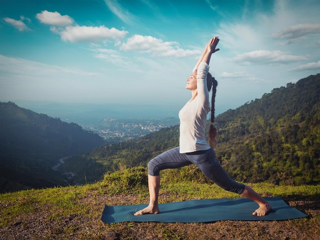 Woman doing yoga asana Virabhadrasana 1 Warrior pose outdoors