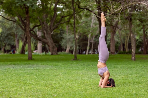 Woman doing yoga asanas in the park on the grass with trees in the background