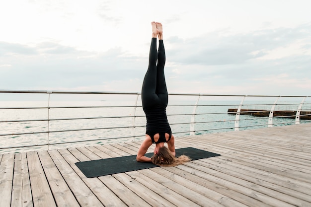 Donna che fa yoga sulla spiaggia e che sta sulle sue mani