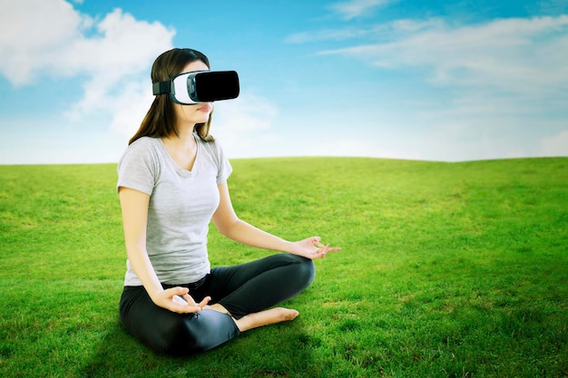 Woman doing yoga exercise with VR glasses at park