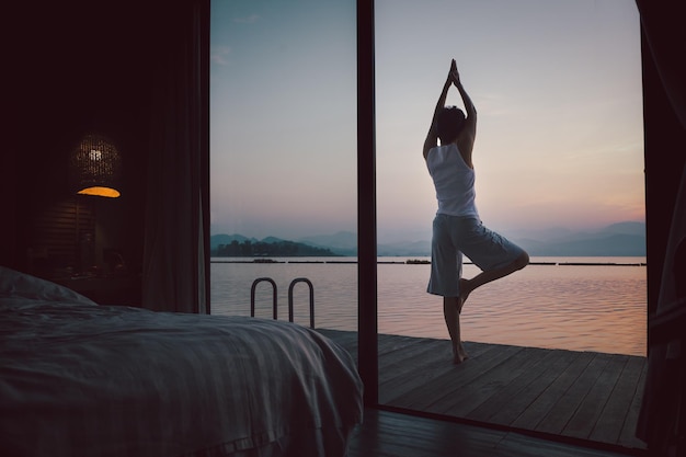 Donna che fa esercizio di yoga sul balcone in legno nella camera da letto all'alba