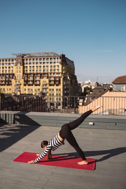 Woman doing yoga exercises on house roof in early morning