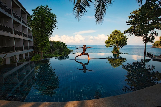 Woman doing yoga near the swimming pool. warrior yoga pose\
against