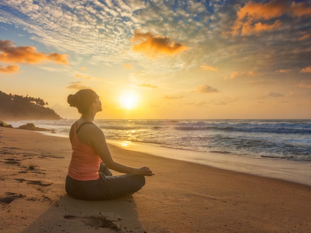 Donna che fa i oudoors di yoga alla spiaggia - posa del loto di padmasana