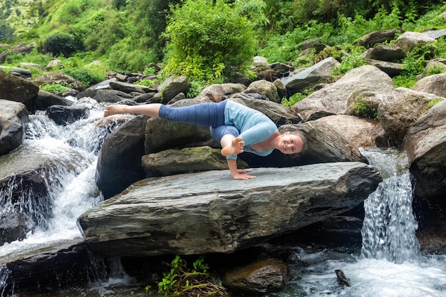 Woman doing yoga oudoors at tropical waterfall