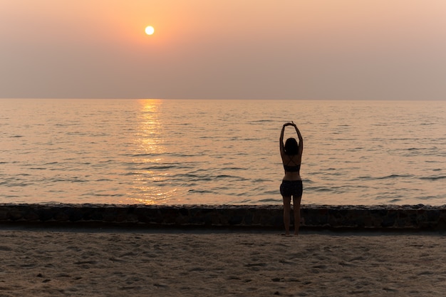 女性休暇でビーチで夕暮れ時ヨガをやっています。