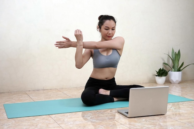 A woman doing yoga with laptop from home