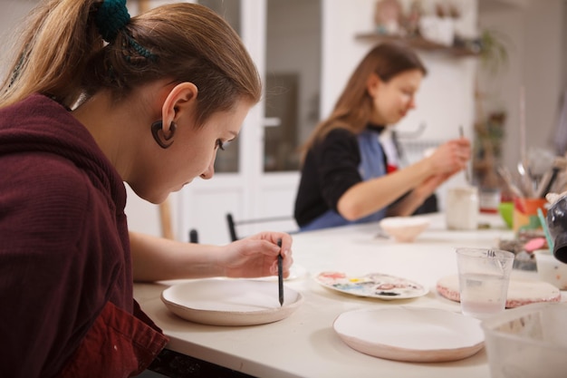 Woman drawing on a ceramic plate, working at pottery scool