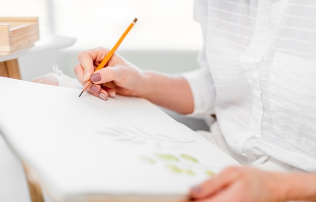 写真 彼女の手に黄色の鉛筆を持って白い紙の帆布にスケッチを描く女性