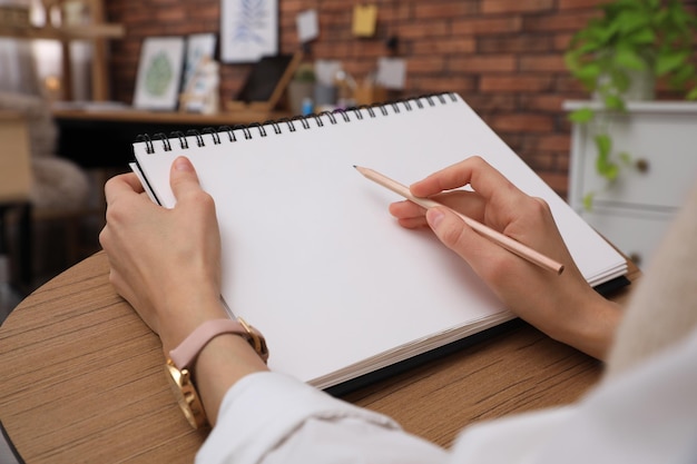 Woman drawing in sketchbook with pencil at home closeup