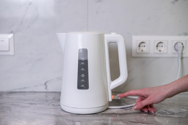 A woman draws water into an electric kettle in the background of the kitchen It's time for breakfast and tea Modern electric kettle Kettle for boiling water