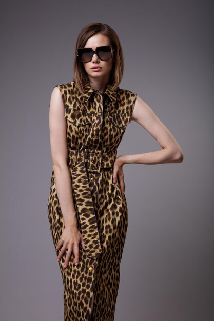 Woman in dress animal leopard print black ankle boots sunglasses on gray background Slim figure